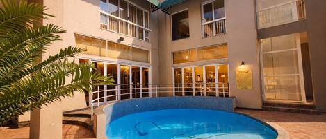 Un hotel con piscina central, varios balcones y un patio de ladrillo.