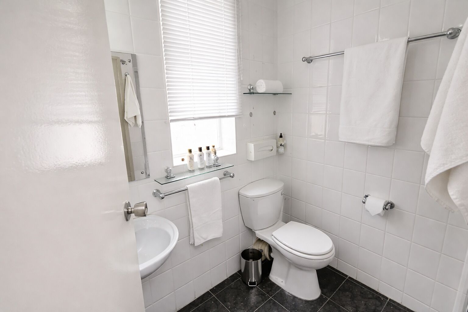 A modern bathroom with a toilet, sink, and glass shelf with toiletries.