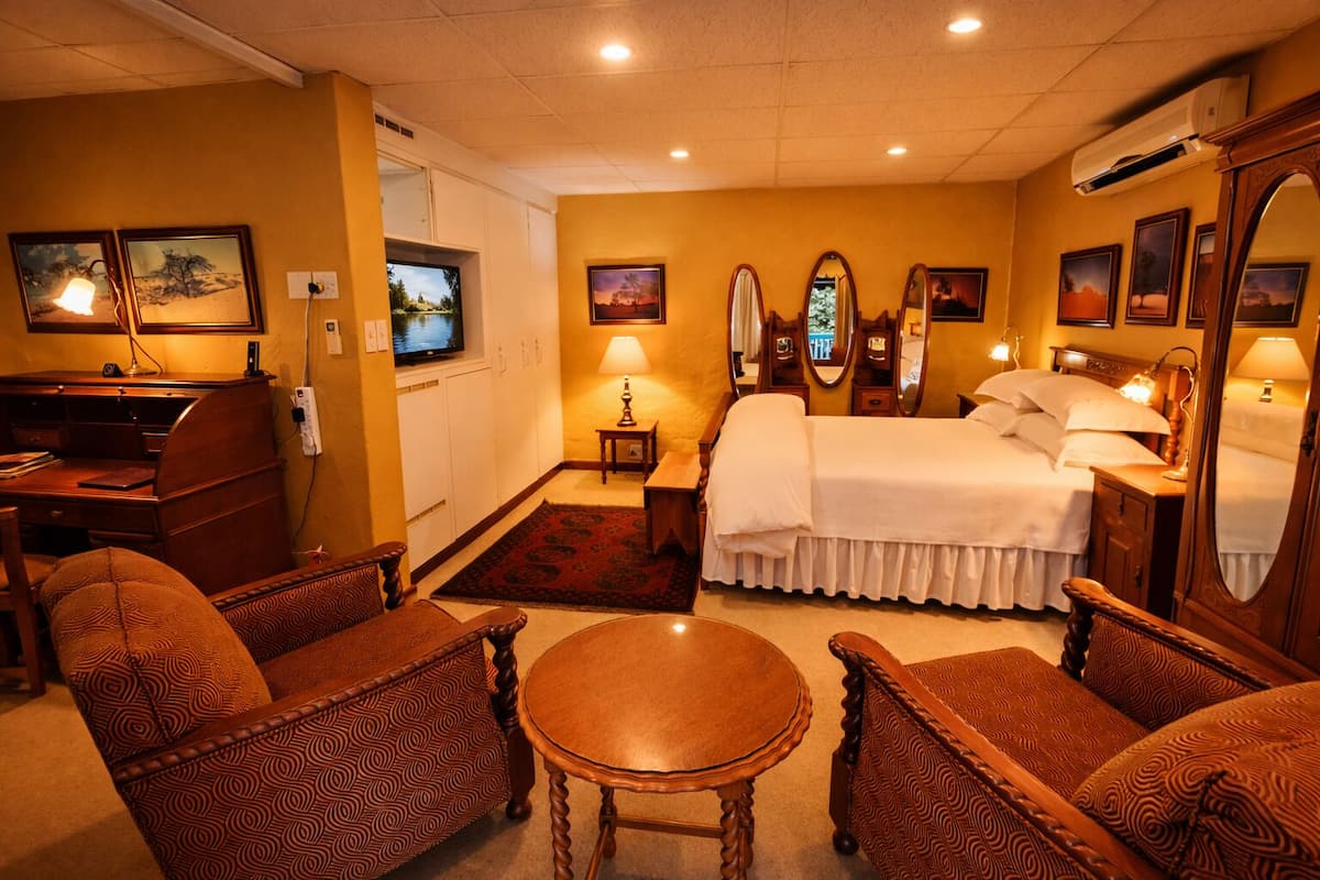 A hotel room with a bed, a desk, a chair, a round table, and a TV.