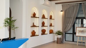 A reception area with a blue counter, terracotta vases on shelves, a potted plant, and a painting on easel. - Hotel SHOL Ninh Chu (Ninh Chu)