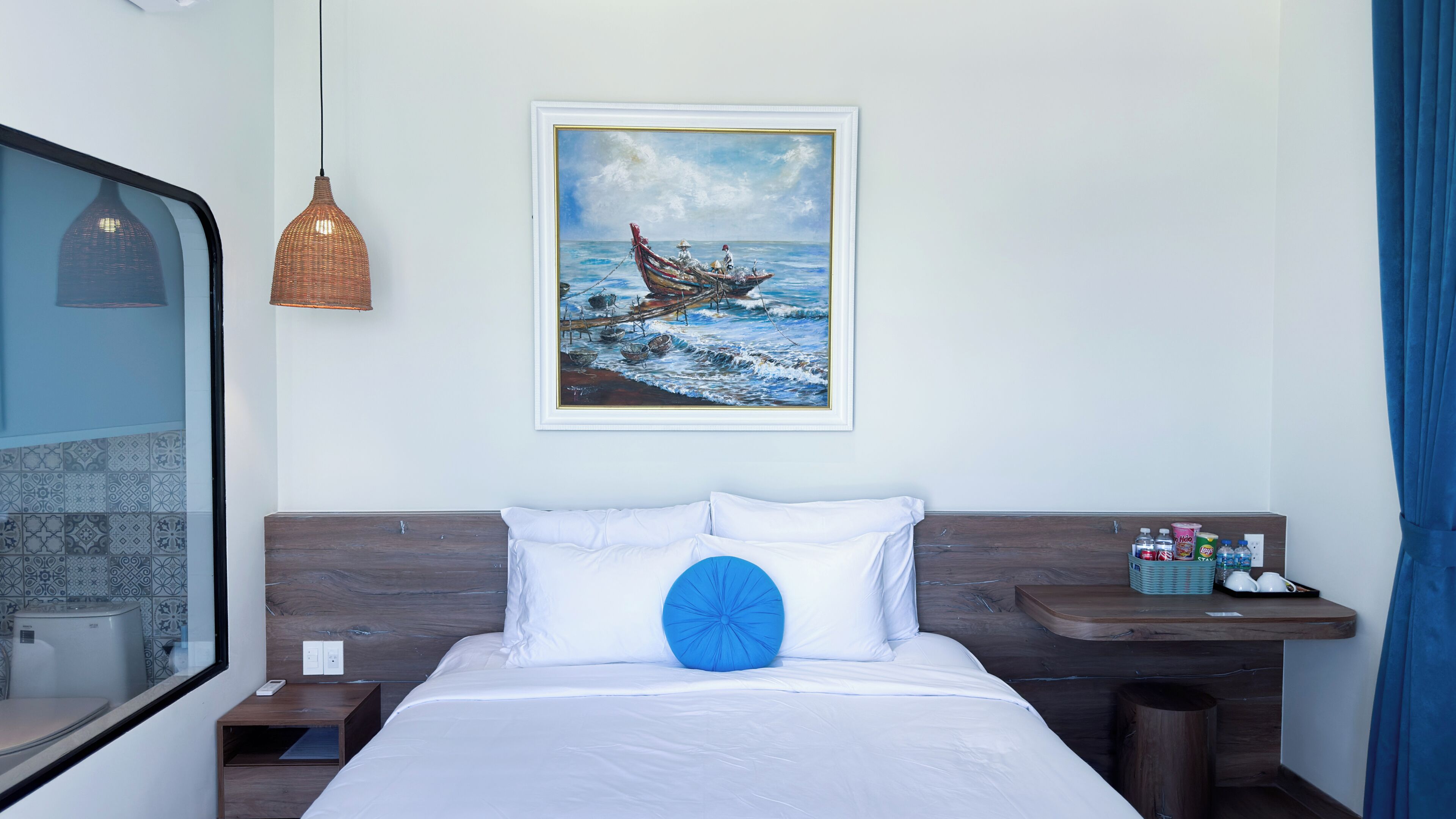 A hotel room with a bed, a nightstand, a painting of a boat on the wall, and a window with a view of a building.