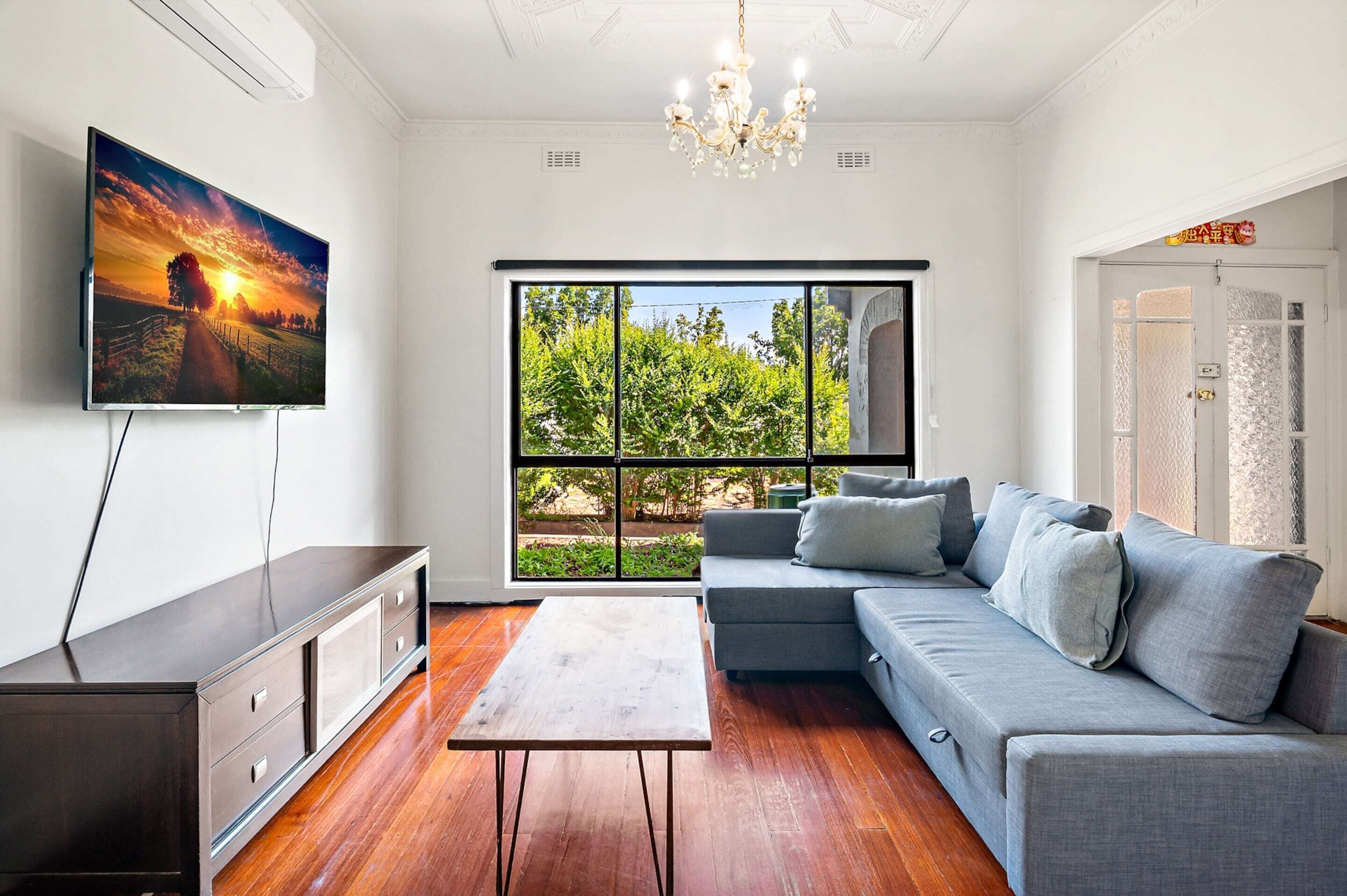 A living room with a TV, sofa, coffee table, and a large window with a view of greenery.