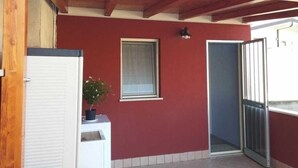 Ein überdachter Außenbereich mit roter Wand, einem Fenster, einer Tür und einer kleinen Pflanze.