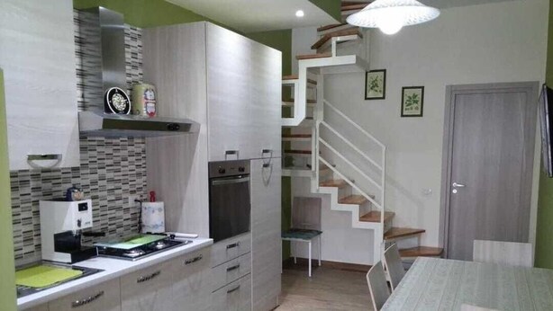 Eine kompakte Küche mit Einbauherd, Mikrowelle und Spüle. Ein Essbereich mit Tisch und Stühlen ist ebenfalls vorhanden. Eine Treppe führt auf eine obere Ebene.