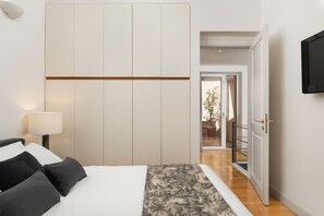 Ein modernes Hotelzimmer mit einem Bett, einem Nachttisch mit Lampe, einem Kleiderschrank und einem an der Wand befestigten Fernseher.