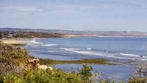 A coastal landscape with a beach, ocean waves, and distant hills. - Wine Region Coastal Retreat on The Esplanade (Adelaide)