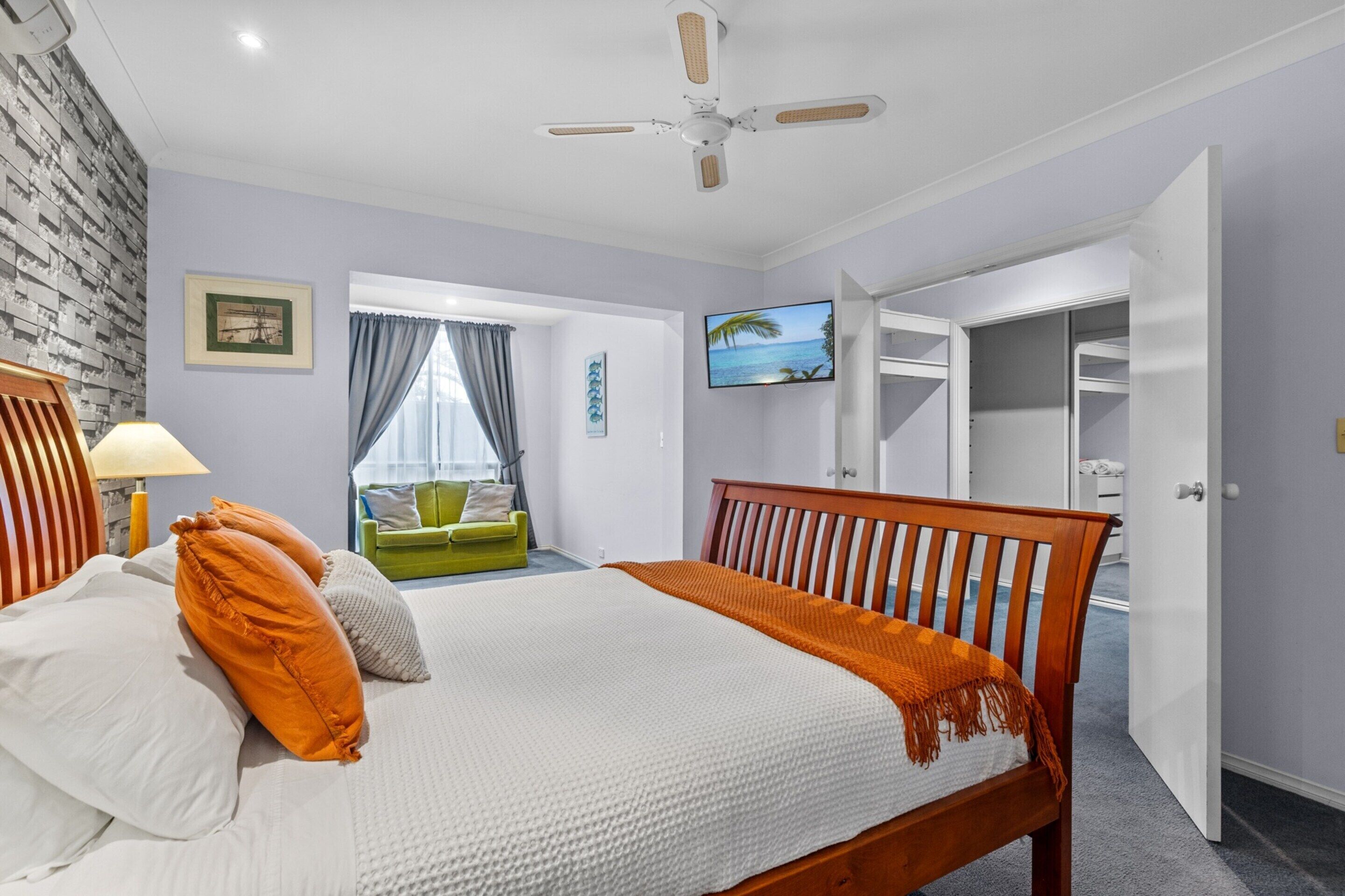Une chambre à coucher avec un lit, un ventilateur de plafond, une télévision et une vue sur l’extérieur par une fenêtre.