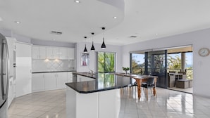 A modern kitchen with white cabinetry, a central island, and pendant lighting. - Wine Region Coastal Retreat on The Esplanade (Adelaide)