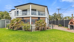 A two-story modern house with a balcony, surrounded by a well-maintained lawn and palm trees. - Wine Region Coastal Retreat on The Esplanade (Adelaide)
