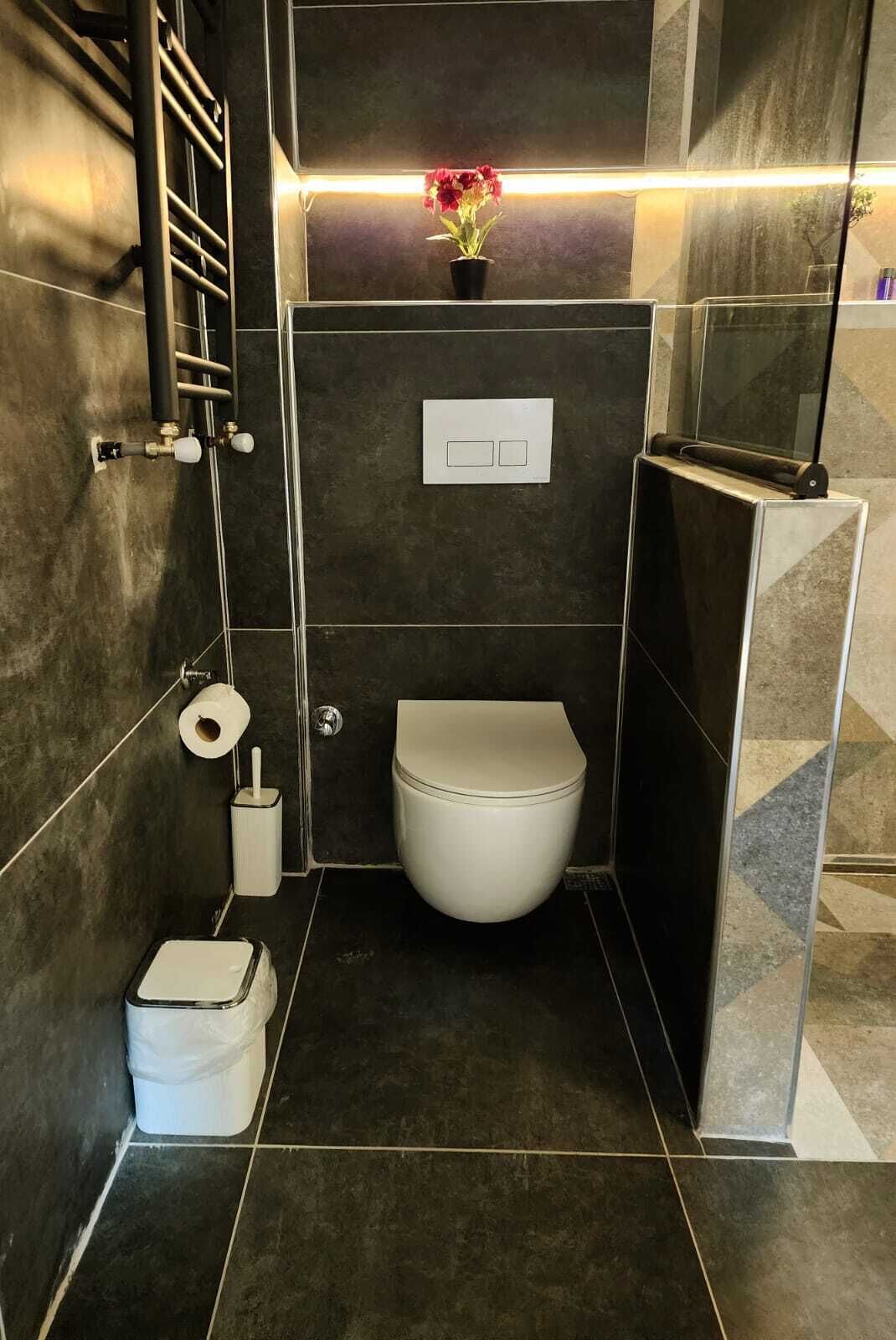 Un bagno piccolo e funzionale con il water, un cestino, un porta rotolo di carta igienica e un lampadario a parete.