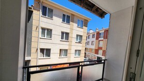 Un balcon avec une balustrade en métal, une vue sur des immeubles à plusieurs étages et un ciel bleu dégagé.
