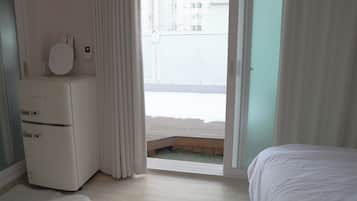Una camera da letto con un letto, una cassettiera bianca, una finestra con tende e vista sugli edifici.
