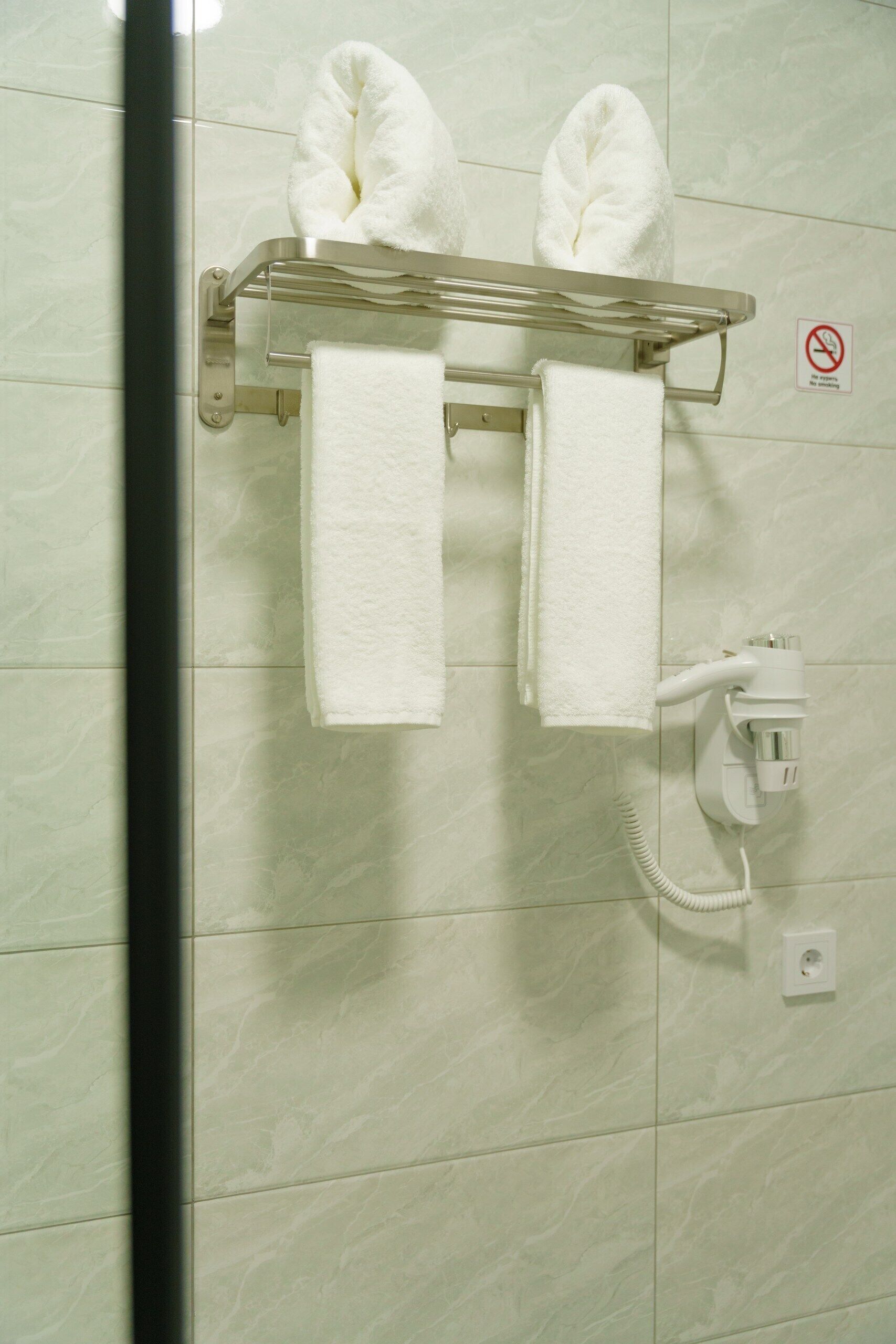 A bathroom with a towel rack holding two towels, a no-smoking sign, and a wall-mounted phone.
