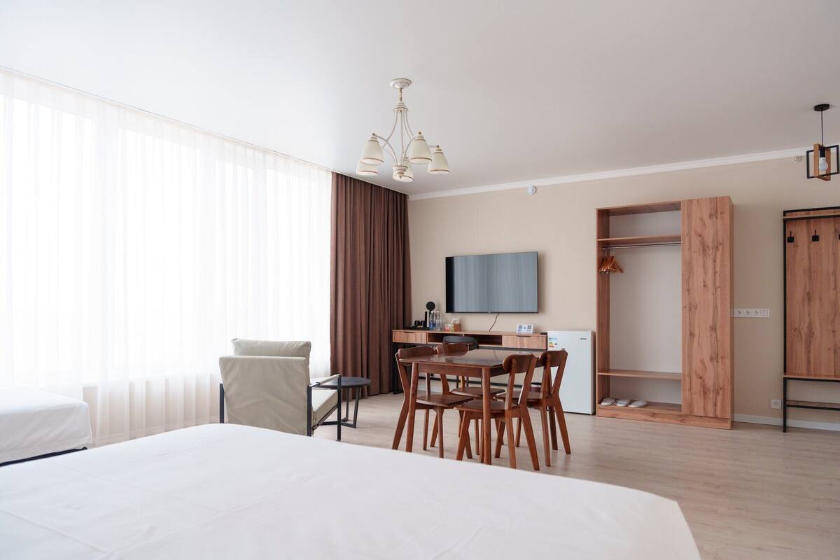 A hotel room with a large bed, a desk with a chair, a television, and a wardrobe.