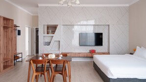 Una habitación de hotel moderna con una cama grande, un televisor fijado en la pared, una mesa de comedor con sillas y un armario de madera.