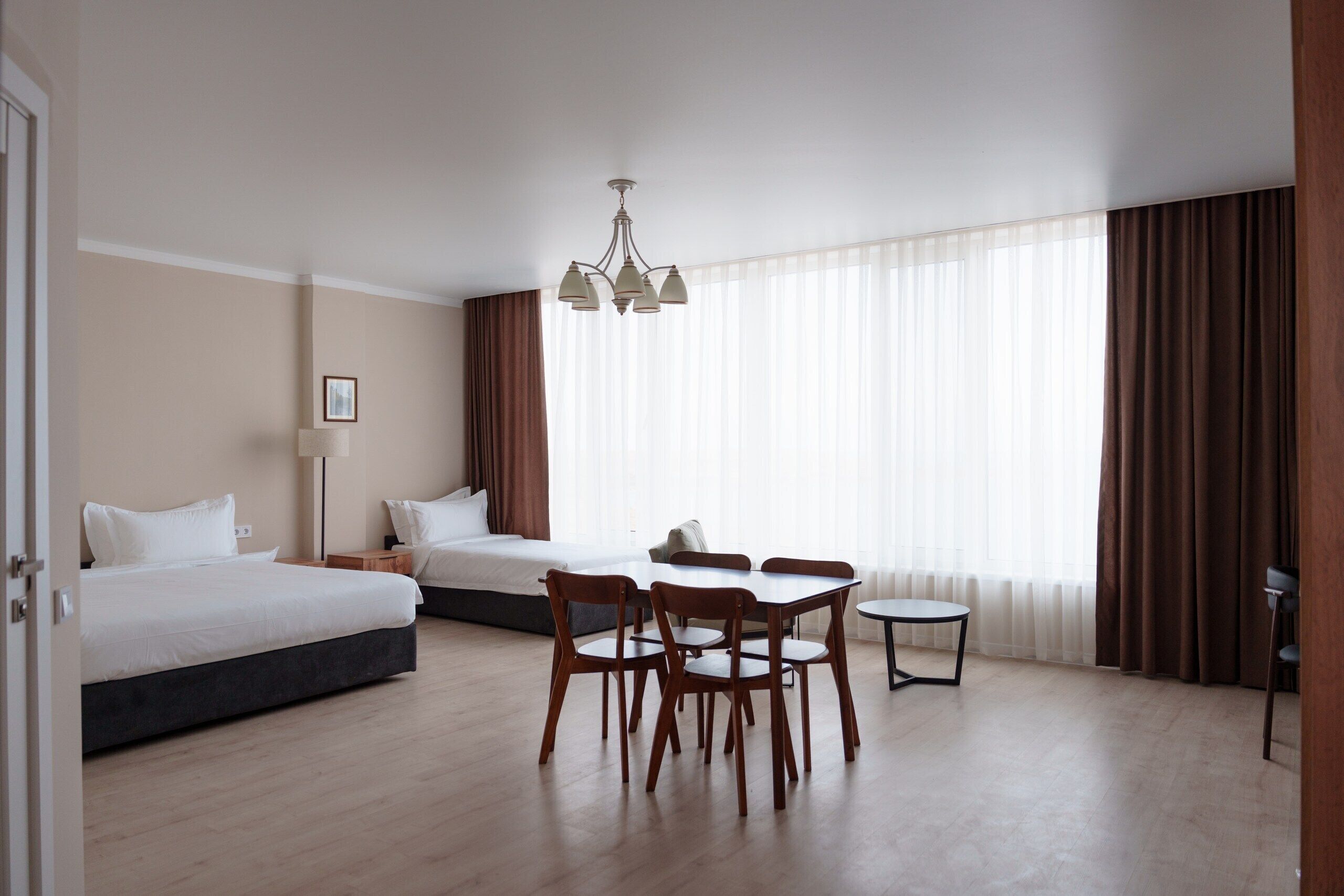 A hotel room with a bed, a desk with chairs, a small table, and a chandelier.