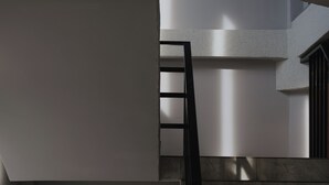 Una escalera con barandilla de metal que lleva a un rellano con pared blanca y una ventana.