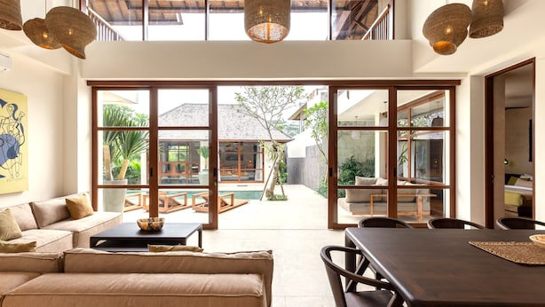 A spacious living area with a large window, a sofa, a dining table, and hanging wicker lamps. - Villa Nordoy 2 by Alfred in Bali (Tabanan)