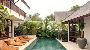 A pool with wooden loungers, surrounded by lush tropical plants, and a large vase on the right. - Villa Nordoy 2 by Alfred in Bali (Tabanan)