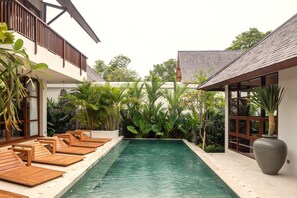 Ein Pool mit Holzliegen, umgeben von üppiger tropischer Vegetation und einer großen Vase auf der rechten Seite.