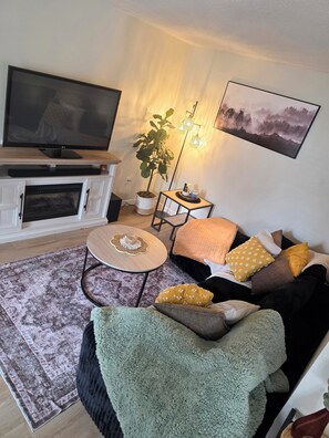 Ein Wohnzimmer mit Fernseher, Kamin, Sofa, Couchtisch und Kunstwerken.