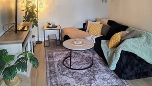 En hyggelig stue med sofa, rundt sofabord, sofabord, et tæppe og en plante.