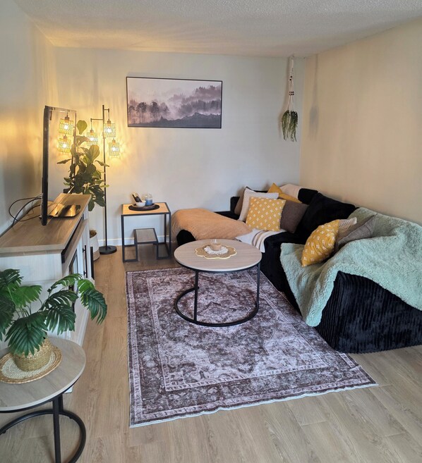 Ein gemütliches Wohnzimmer mit einer Couch, einem kleinen runden Tisch, einem Couchtisch, einem Teppich und einer Pflanze.