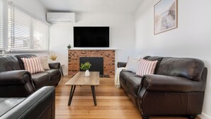 Ein Wohnzimmer mit zwei Ledersofas, einem Holztisch, einem Kamin aus Ziegelsteinen und einem an der Wand befestigten Fernseher.