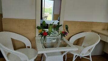 Una habitación con una mesa de vidrio, dos sillas blancas de mimbre y una mesita con un jarrón de flores.