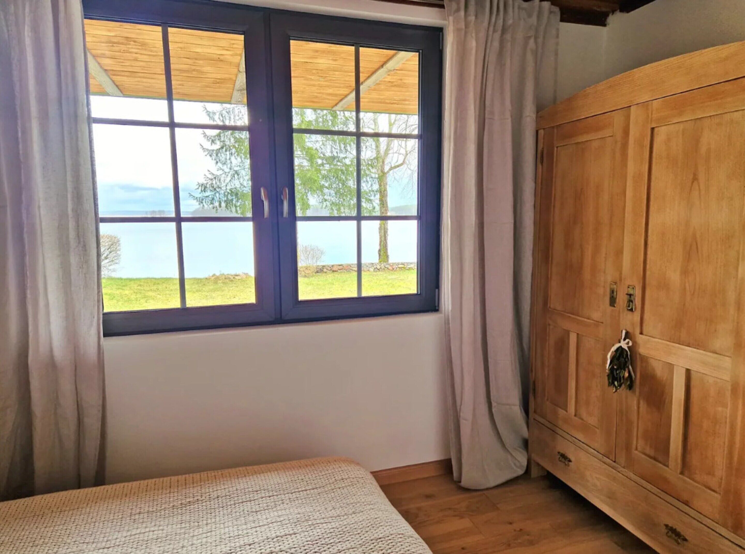 A bedroom with a large window, wooden wardrobe, and a bed.