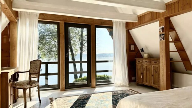 A bedroom with a large window, a chair, a bed, and a wooden cabinet. - Holiday Villa With Sauna, on the Shore of the Lake (gmina Osiek)