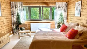 A wooden cabin bedroom with a bed, a chair, a desk, and a window with curtains. - Holiday Villa With Sauna, on the Shore of the Lake (gmina Osiek)