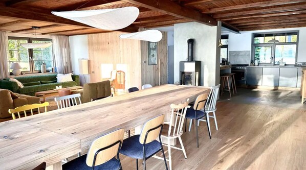 Un vaste espace de vie comprenant une longue table à manger en bois, de nombreuses chaises, un canapé vert et un coin cuisine équipé d’une cuisinière et de placards.