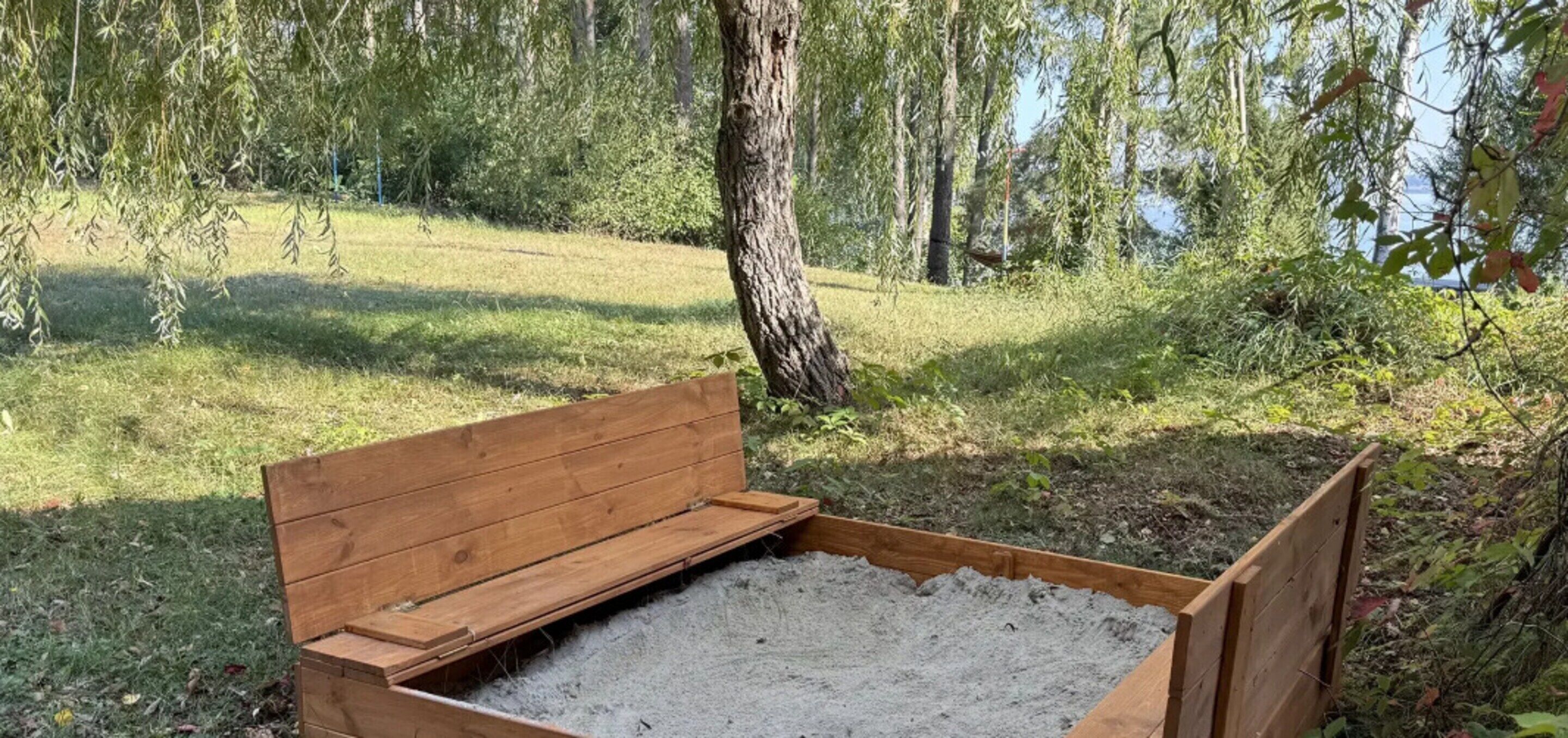 A wooden bench in a natural setting with a grassy area and trees in the background.
