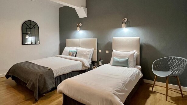 Habitació d'hotel amb dos llits, una cadira moderna, un mirall fixat a la paret i una làmpada al sostre.