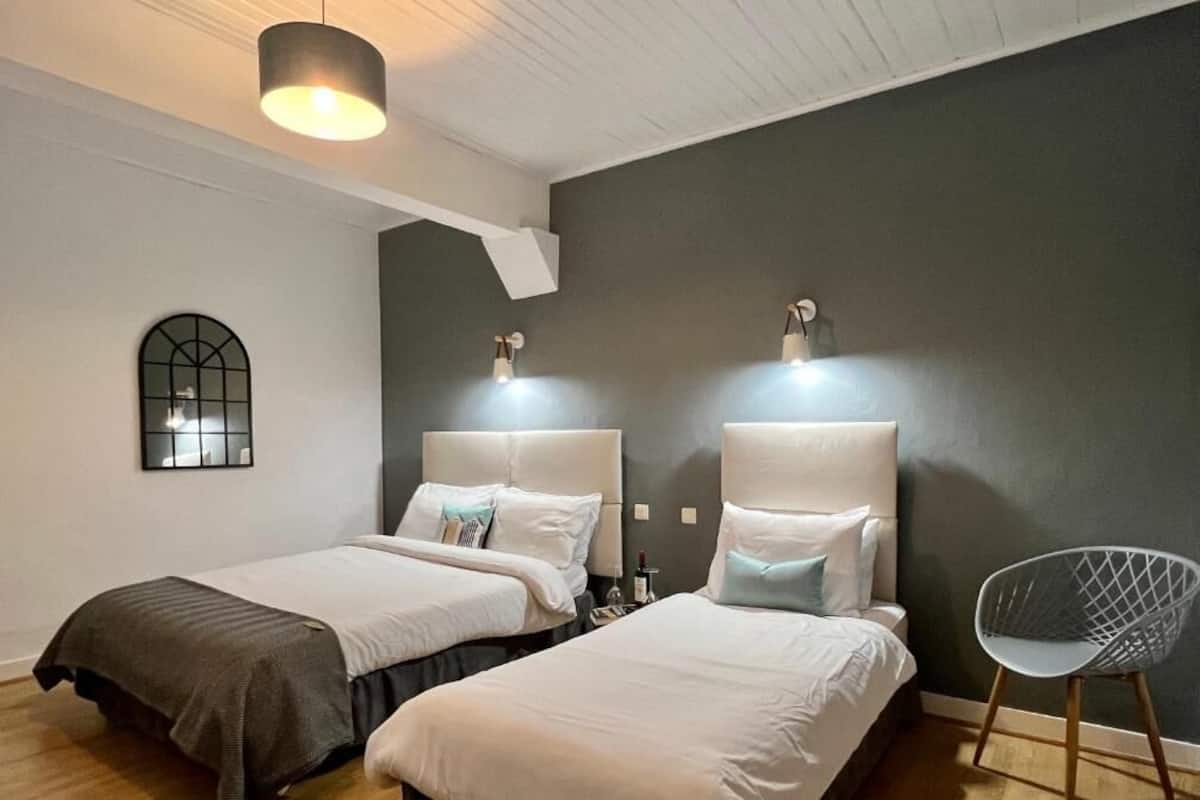 A hotel room with two beds, a modern chair, a wall-mounted mirror, and a ceiling light fixture.