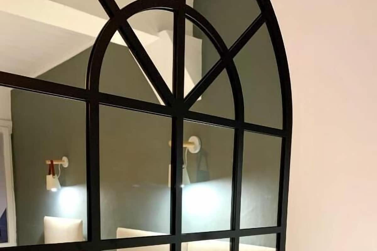 A modern room with a white sofa, a large mirror with a black frame, and a wall-mounted light fixture.