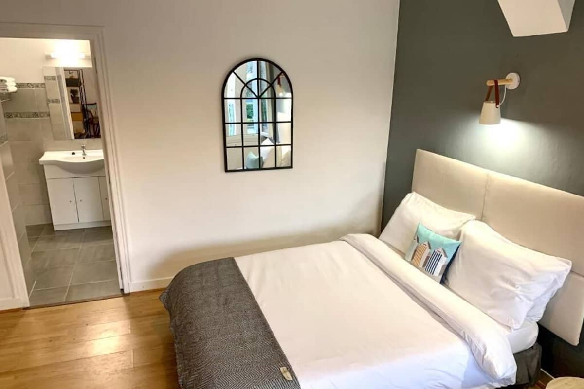 A bedroom with a bed, a nightstand, a mirror, and a wall-mounted light fixture.