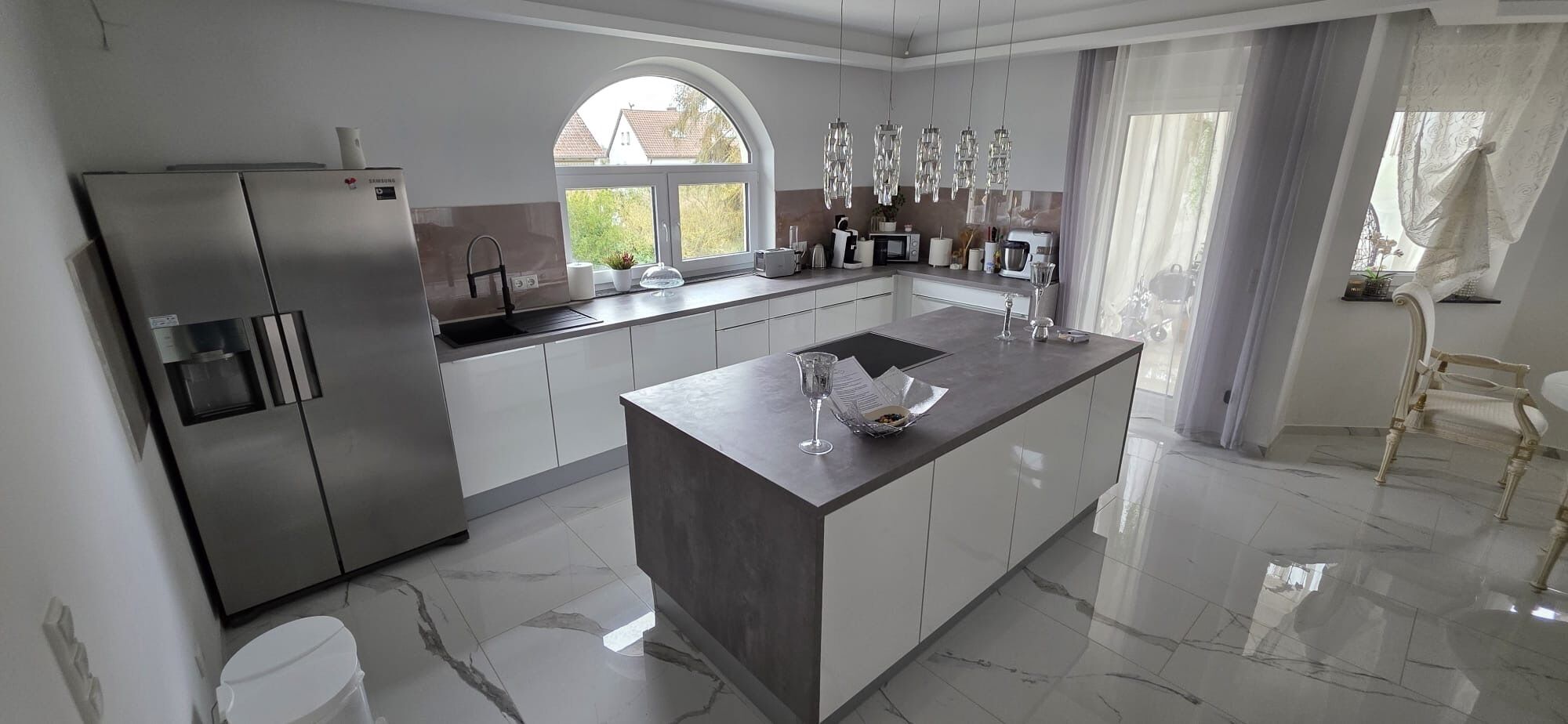 A modern kitchen with a central island, stainless steel appliances, and a view through an arched window.