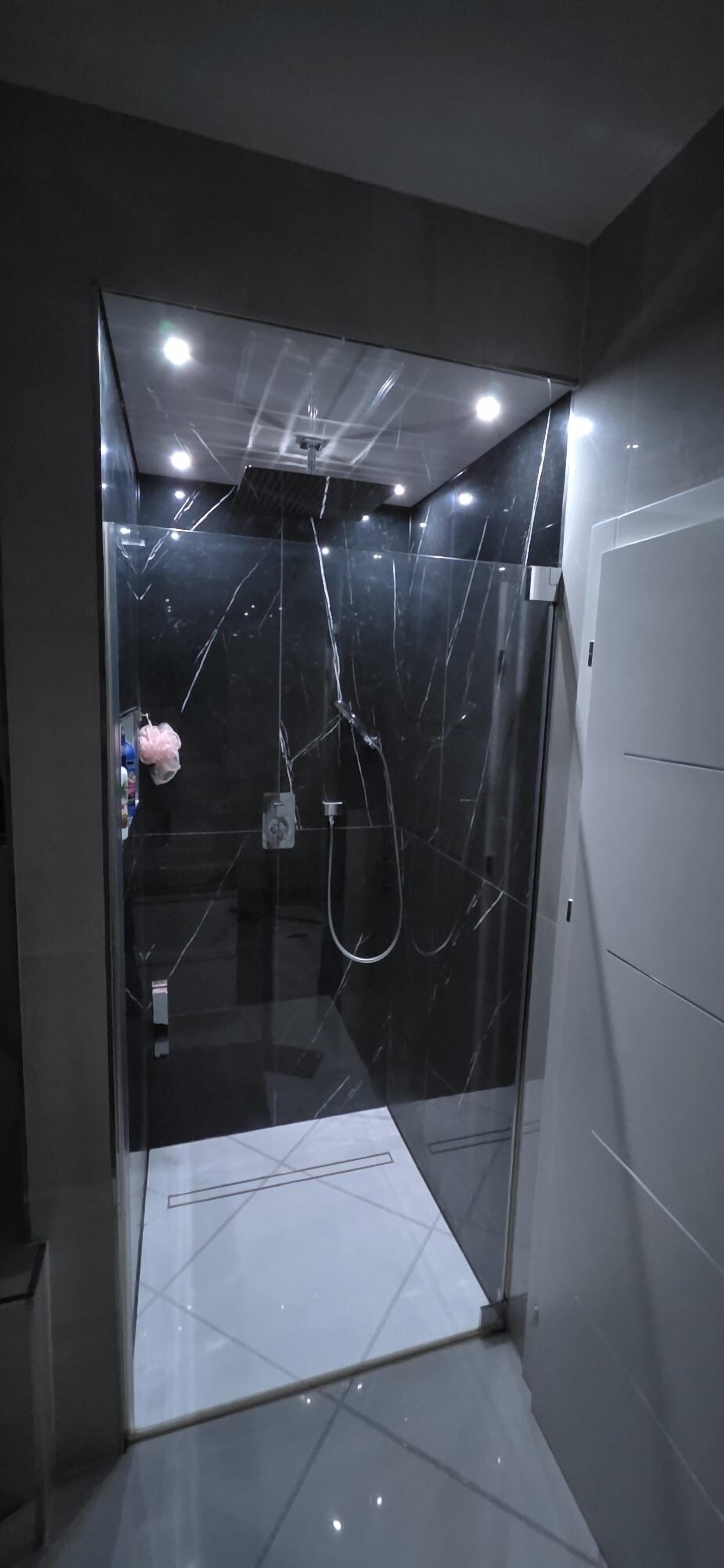 A modern shower enclosure with a glass door, a handheld showerhead, and a visible control panel.