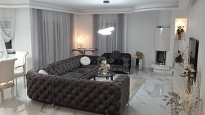 Een moderne woonkamer met een hoekbank, een eethoek met stoelen, een televisie en een open haard.