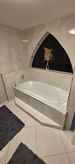 Un baño moderno con una bañera independiente, un jarrón decorativo negro y un tapete blanco y negro.