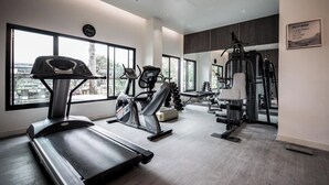 A modern gym with cardio machines, weight equipment, and large windows offering city views. - Aster Residence Rayong (Rayong)