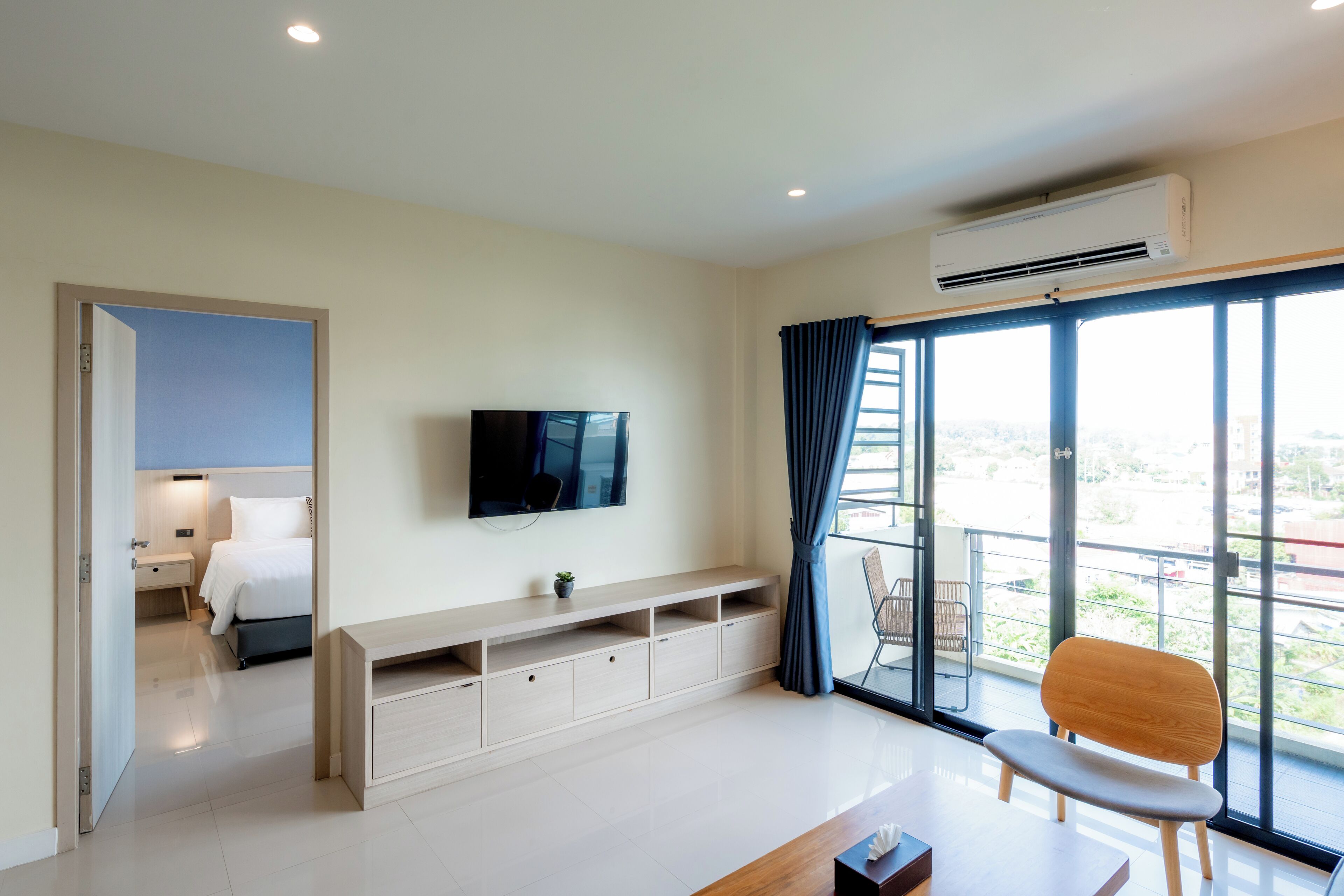 Habitación de hotel moderna con un ventanal grande, televisión de pantalla plana, un banco de madera y balcón con una silla.