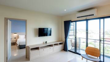 Habitación de hotel moderna con un ventanal grande, televisión de pantalla plana, un banco de madera y balcón con una silla.