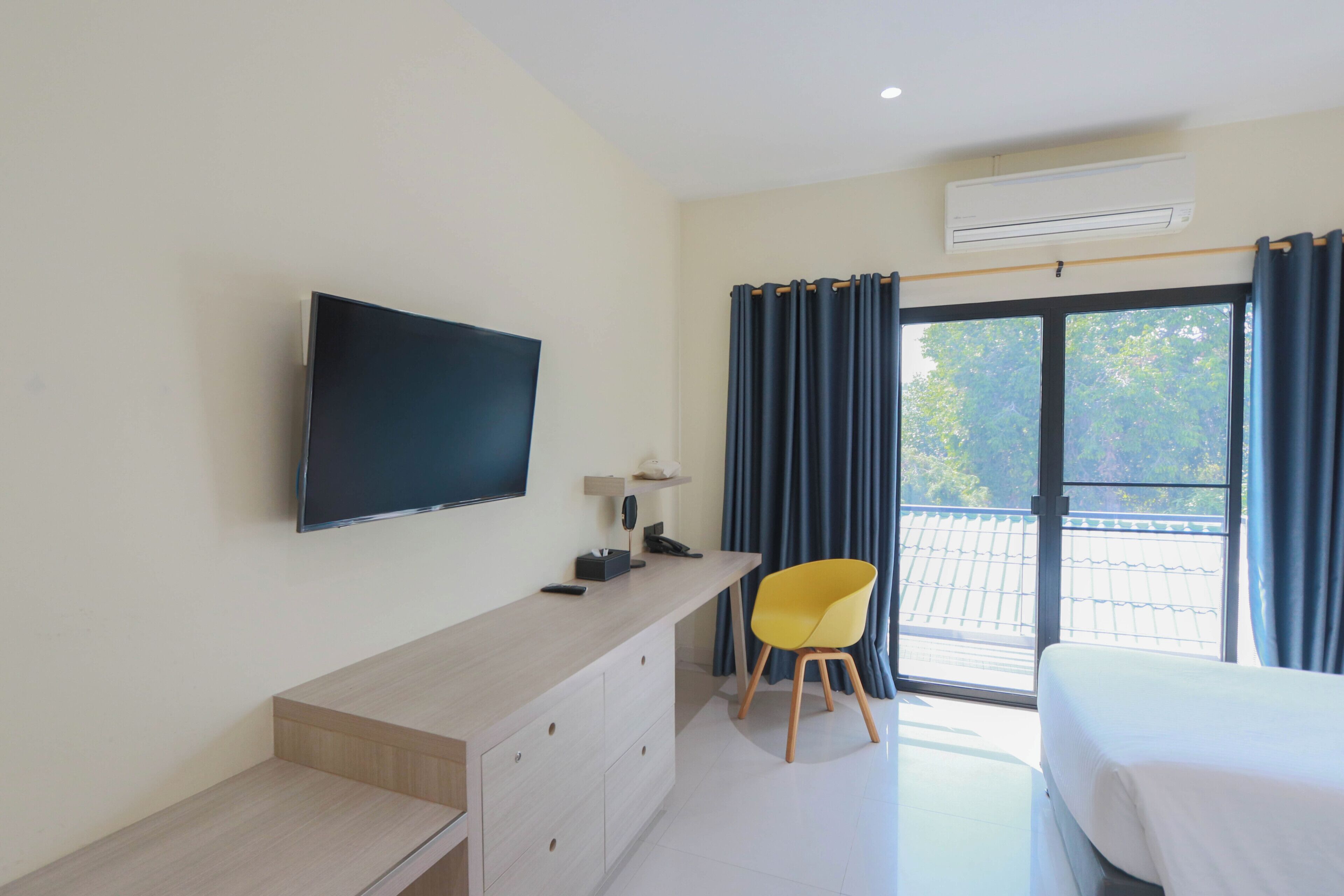 Ein Hotelzimmer mit Bett, Schreibtisch, Flachbildfernseher, Stuhl und Balkon mit Vorhängen.