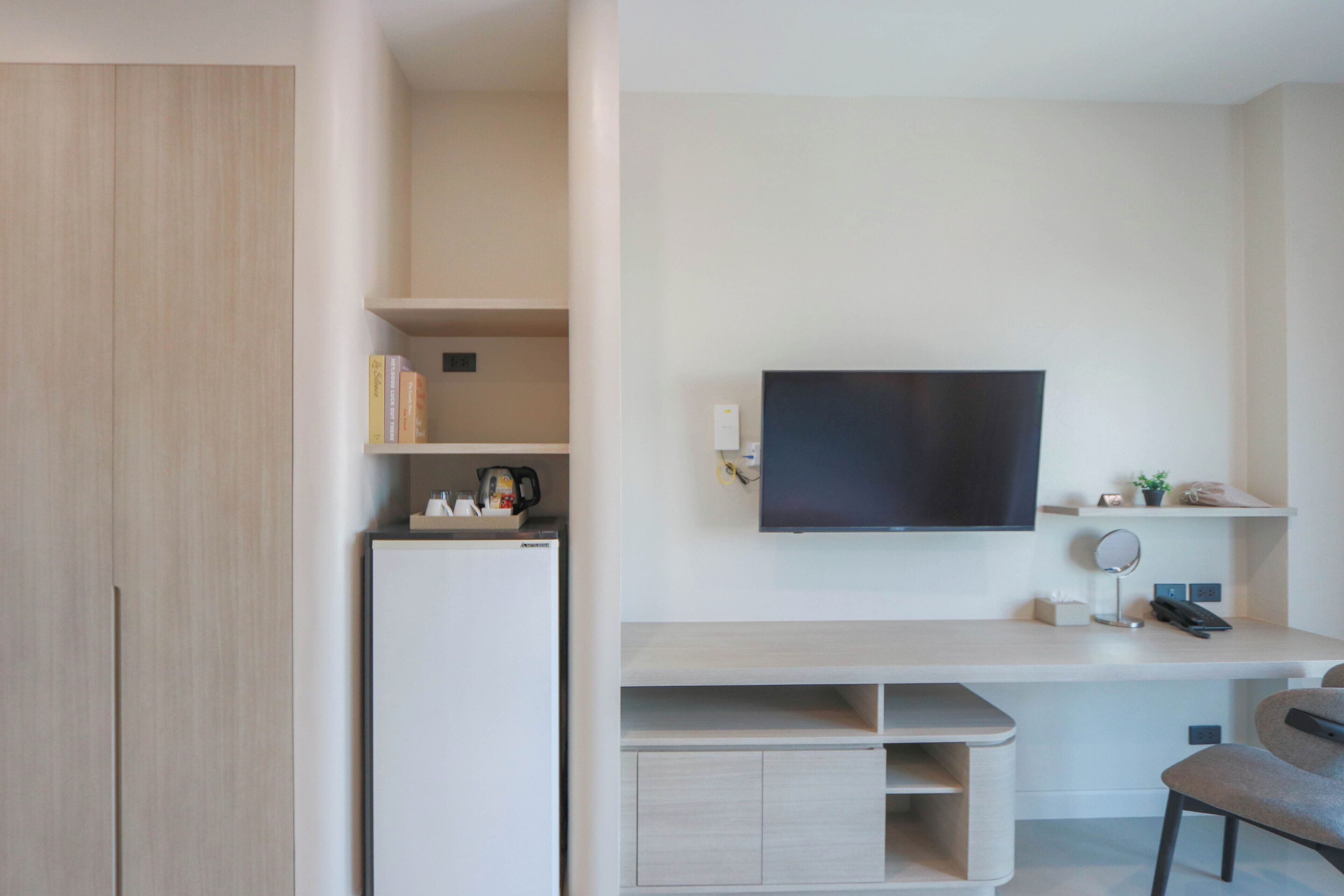 Una habitación moderna con televisión de pantalla plana, escritorio, silla y estanterías integradas.