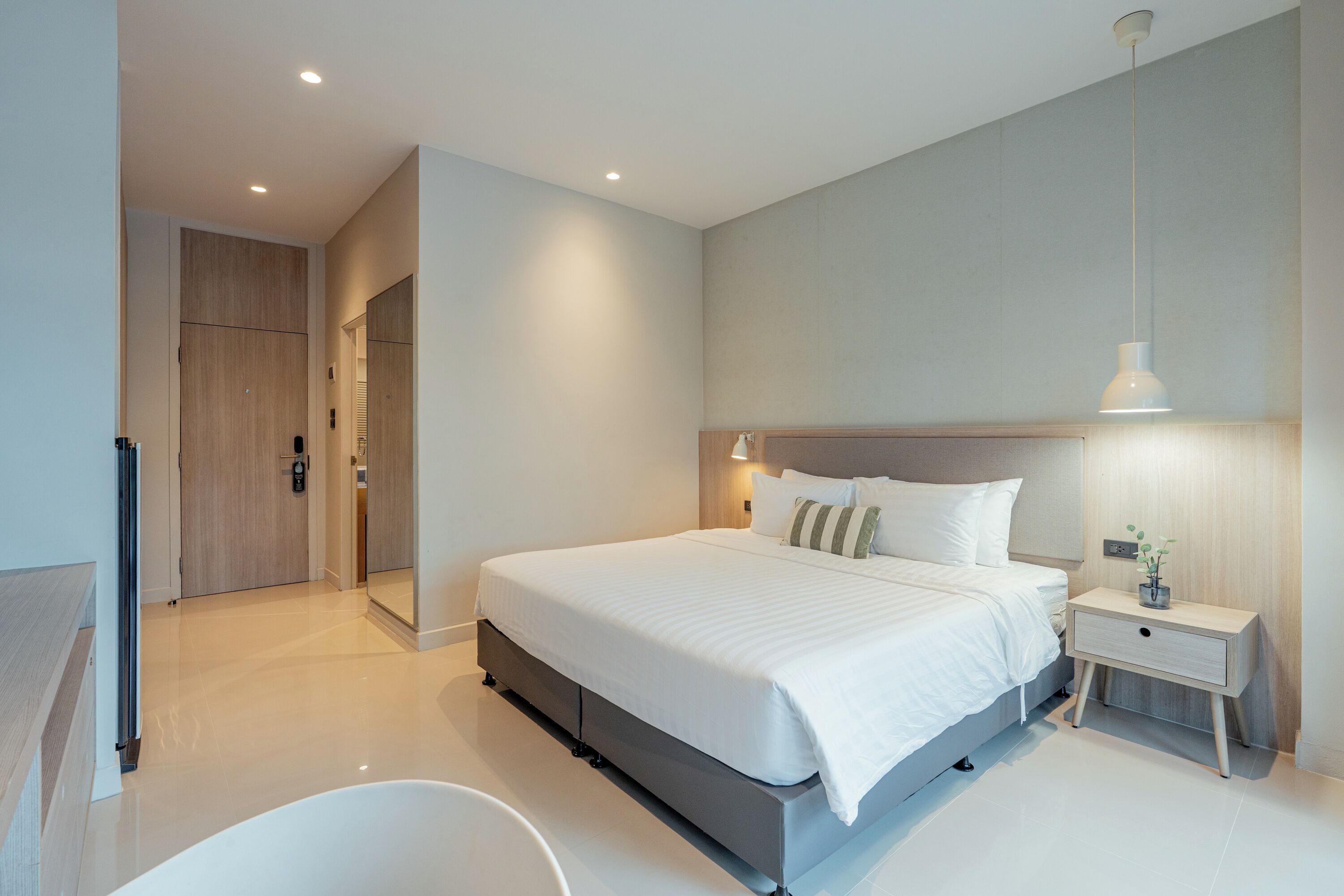 A modern hotel room with a large bed, bedside tables, a mirror, and a bathroom with a bathtub.