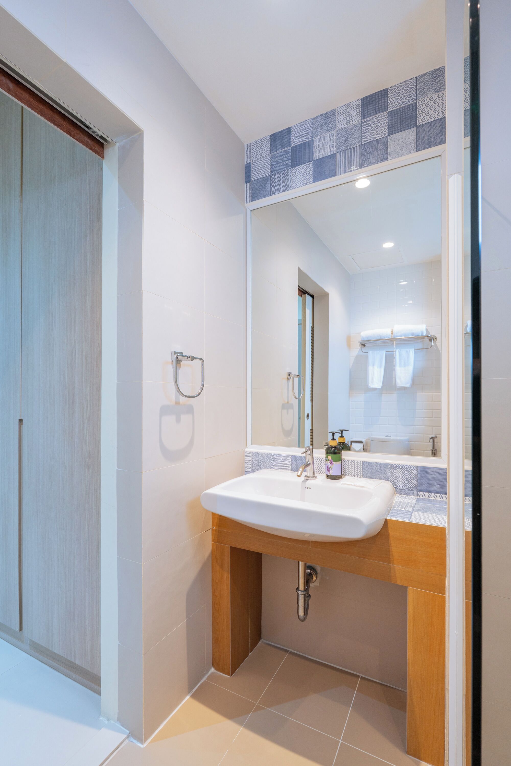 Un baño moderno con un lavamanos blanco, tocador de madera y un espejo grande.