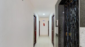 Un couloir avec des portes de part et d’autre, un extincteur fixé au mur et une grille métallique sur le côté droit.